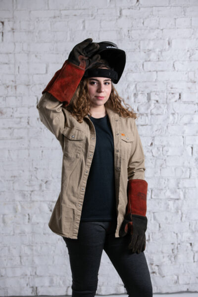Woman wearing a welding helmet, gloves and jacket with Seraphina Safety's Flame Resistant FR t-shirt and legging set underneath.