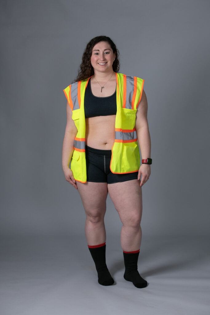 Woman wearing Seraphina Safety's flame resistant FR bra and boy shorts with a construction vest on top.